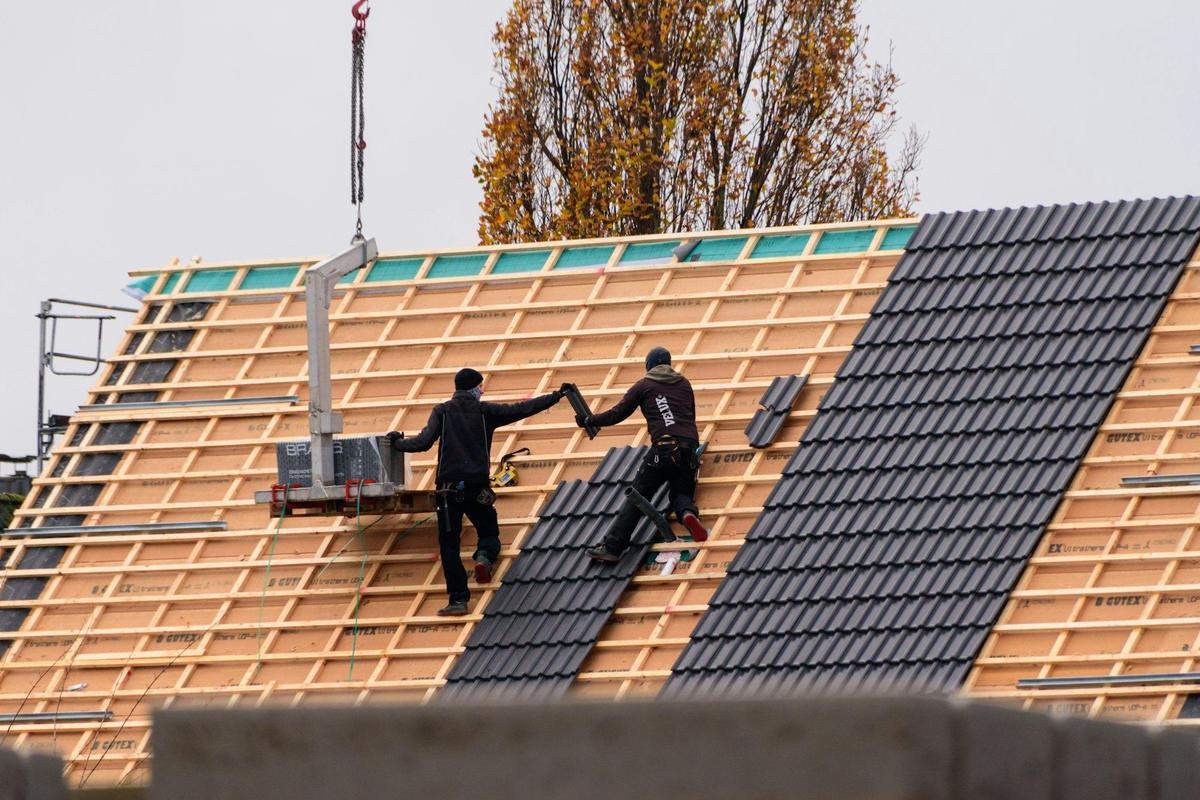 Twee dakwerkers leggen antraciete pannen op nieuwe panlatten